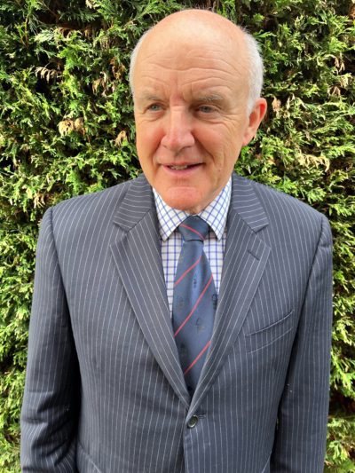 John Robinson in a suit in front of a hedge