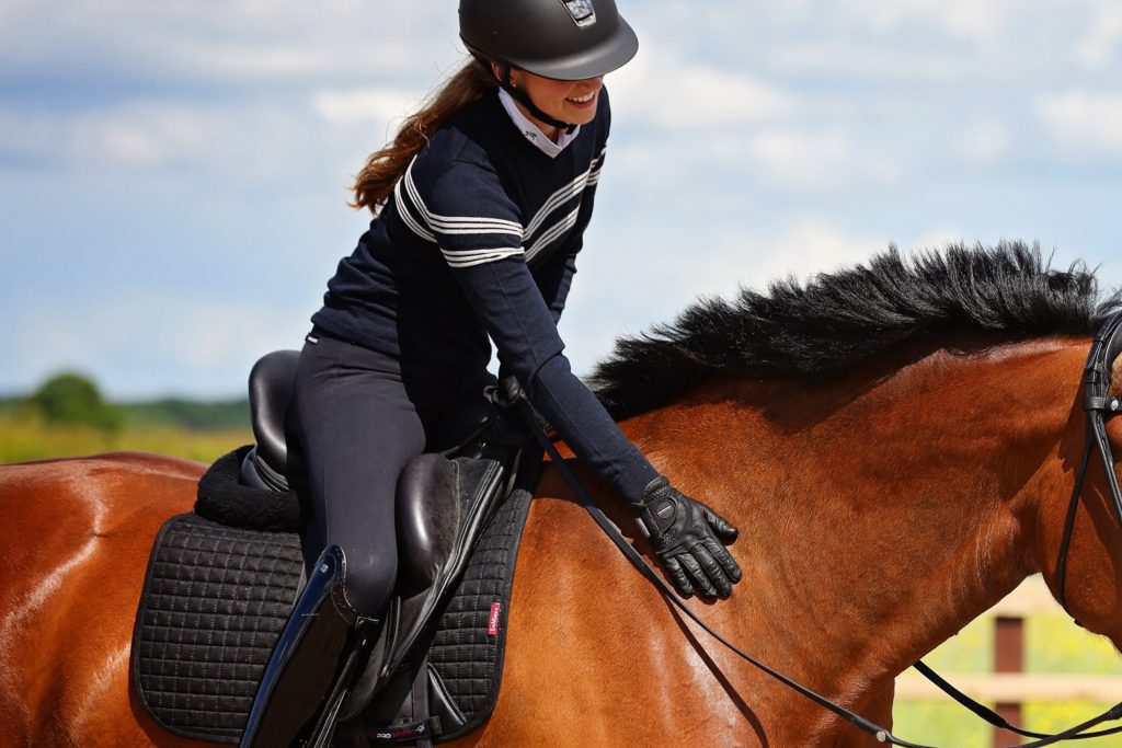 A young woman schooling dressage thanks her bay horse